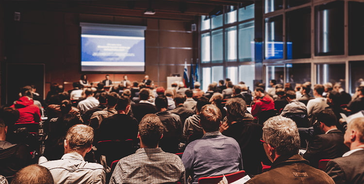 event attendees sit in an audience to watch a presentation on a large screen